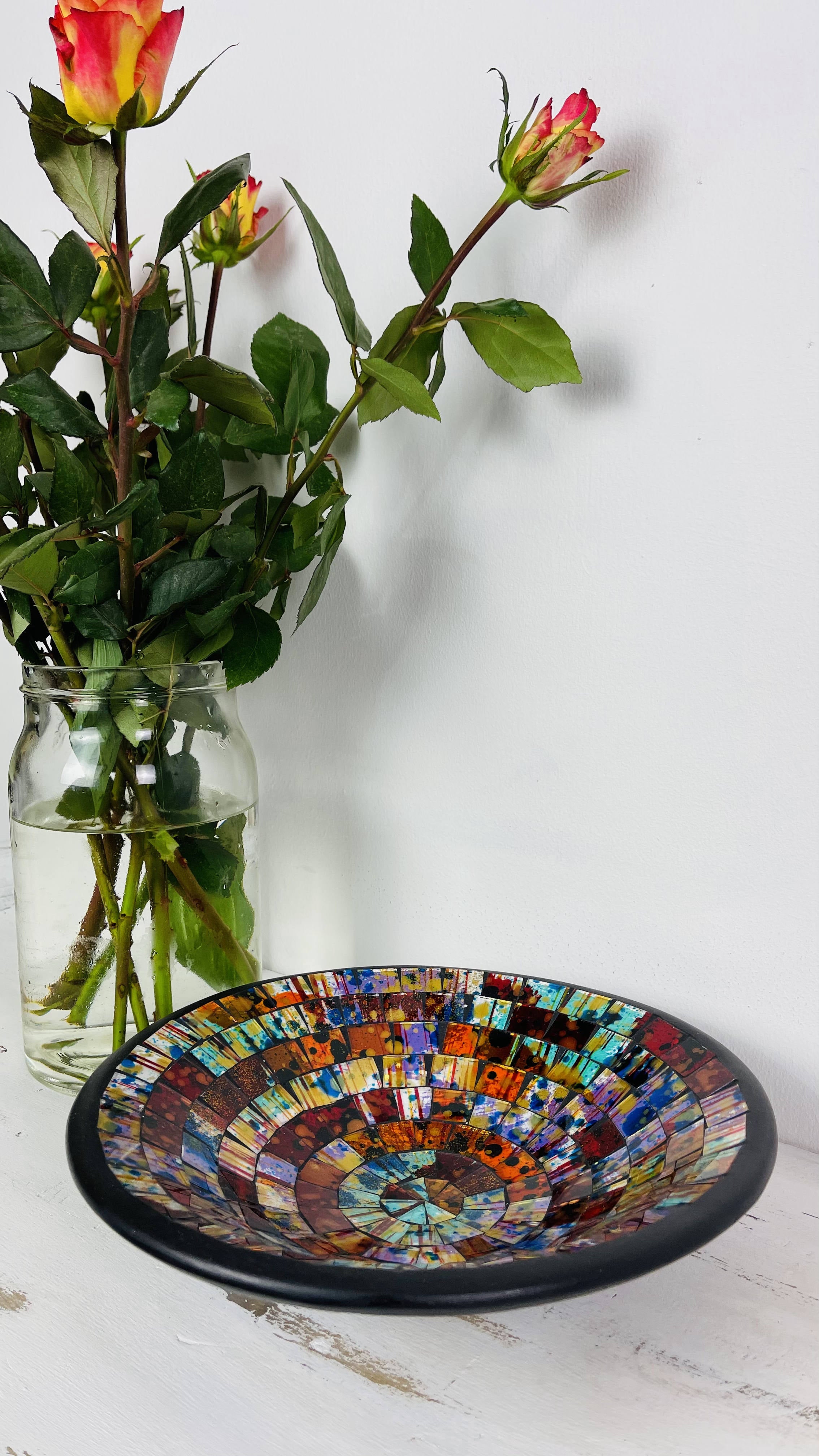 front view of mosaic bowl next to a vase of flowers